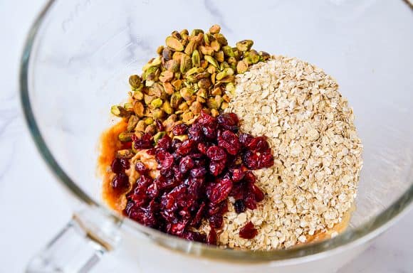 Clear mixing bowl containing quick oats, dried cranberries, pistachios and honey