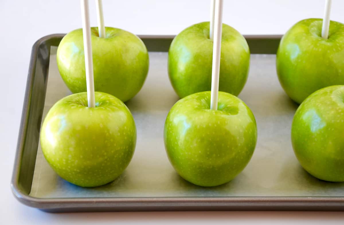 Granny Smith apples with lollipop sticks on a wax paper-lined baking sheet.