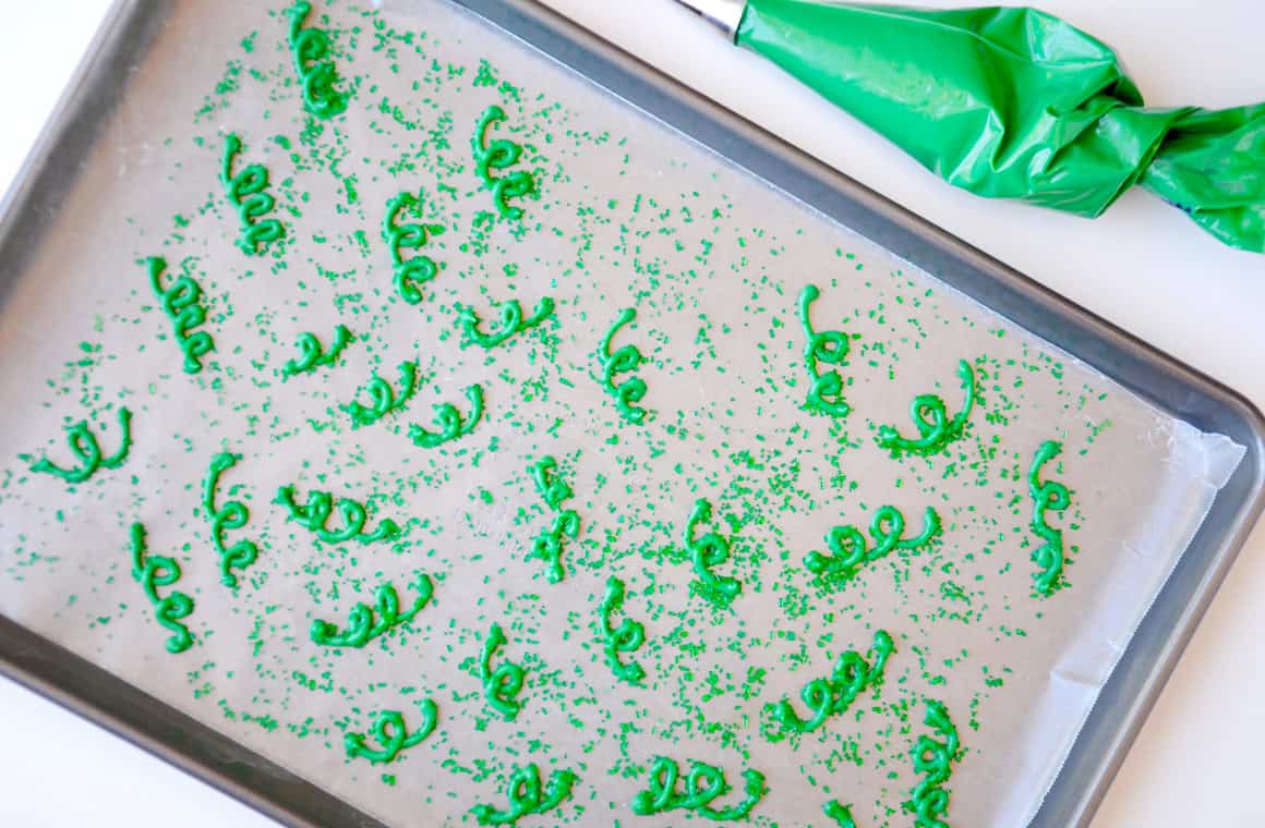 Green candy melts in the shape of vines sprinkled with green sprinkles on a baking sheet.