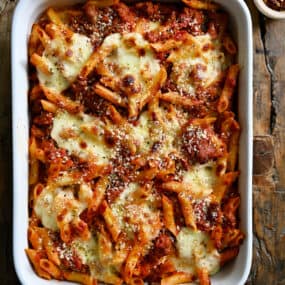 A white baking dish containing baked penne with sausage garnished with grated Parmesan cheese.