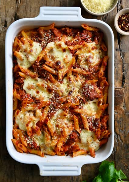 A white baking dish containing baked penne with sausage garnished with grated Parmesan cheese.