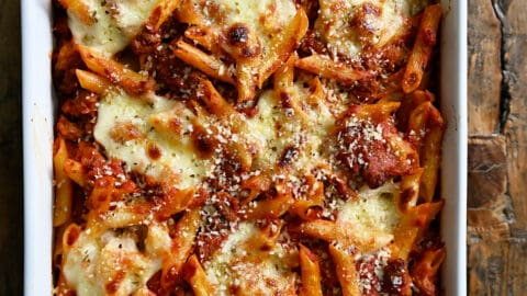 A white baking dish containing baked penne with sausage garnished with grated Parmesan cheese.