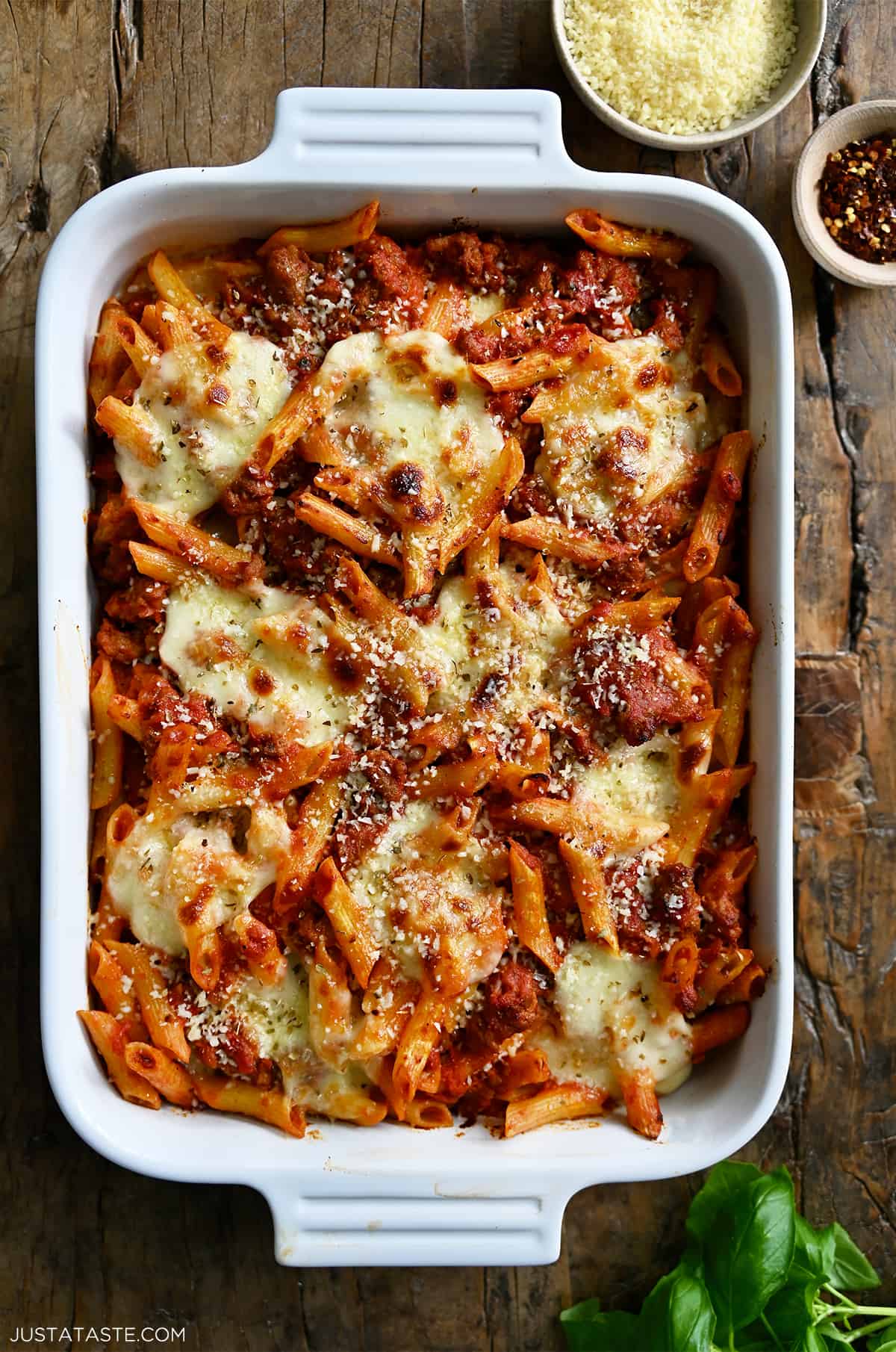 A white baking dish containing baked penne with sausage garnished with grated Parmesan cheese.