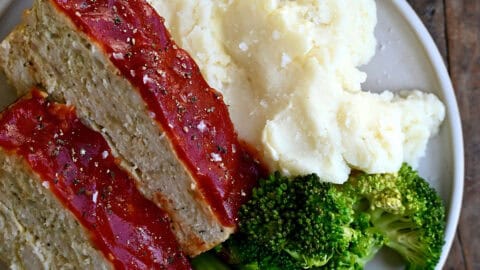 Two slices of classic chicken meatloaf on a dinner plate with steamed broccoli and mashed potatoes.