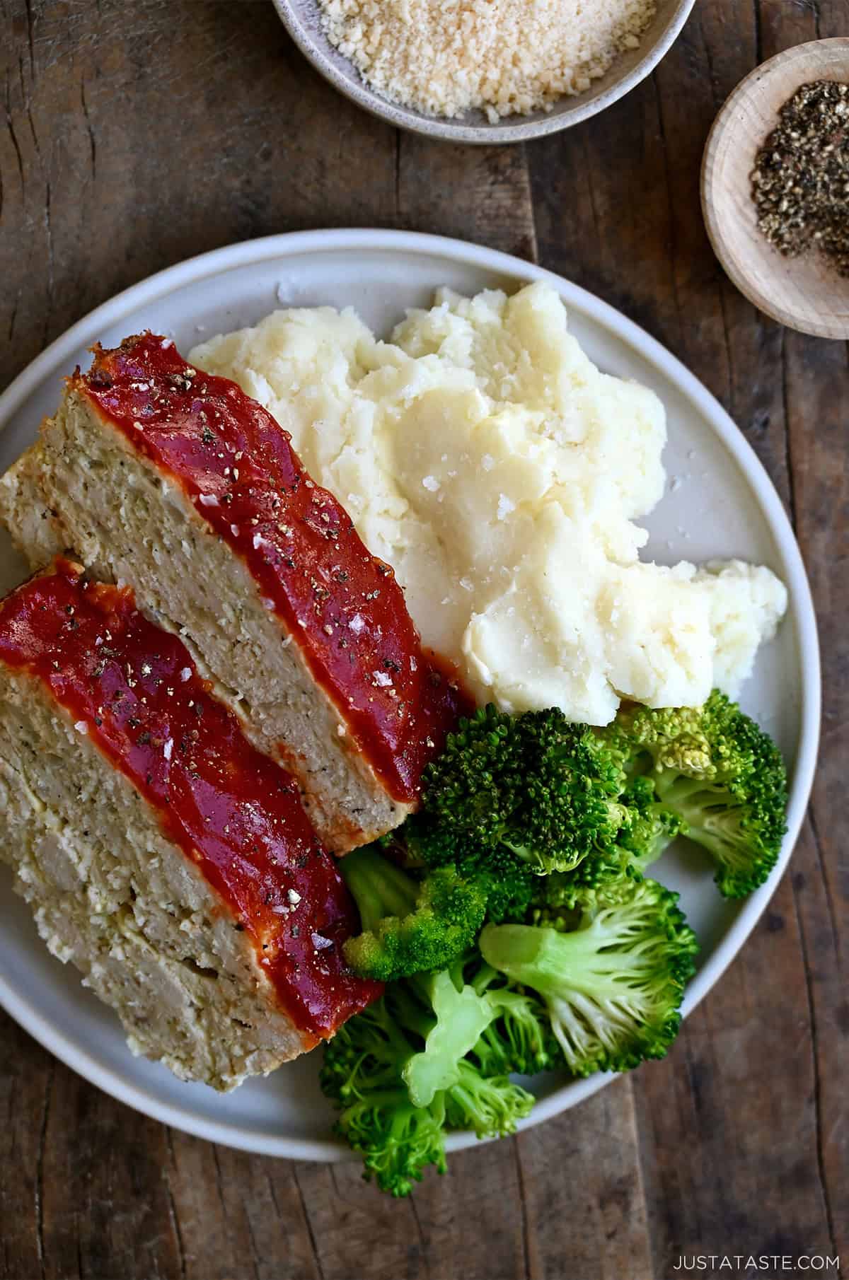 Two slices of classic chicken meatloaf on a dinner plate with steamed broccoli and mashed potatoes.