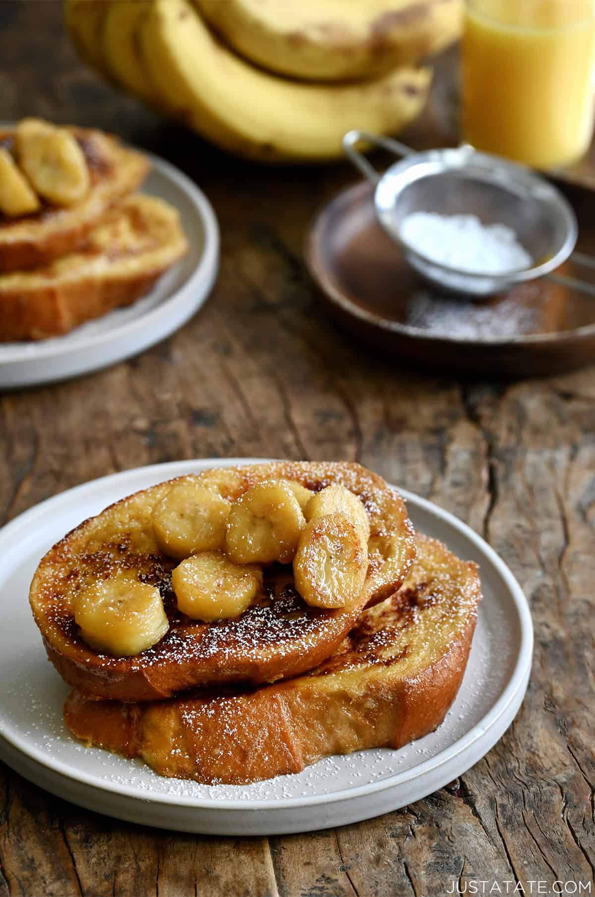 Two slices of French toast topped with caramelized bananas and dusted with powdered sugar.