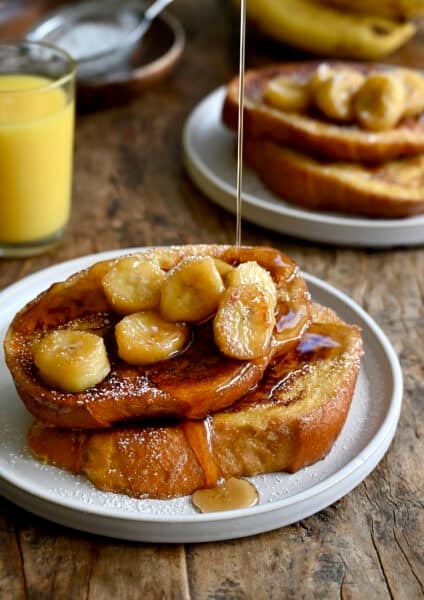 Two slices of French toast topped with caramelized bananas and maple syrup on a plate.