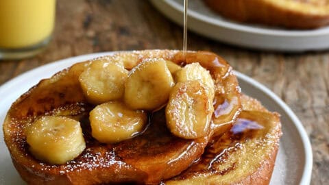 Two slices of French toast topped with caramelized bananas and maple syrup on a plate.