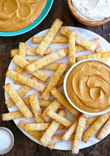 A top down view of pie crust fries on a white platter with bowls of pumpkin dip