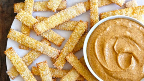 A top down view of pie crust fries on a white platter with bowls of pumpkin dip