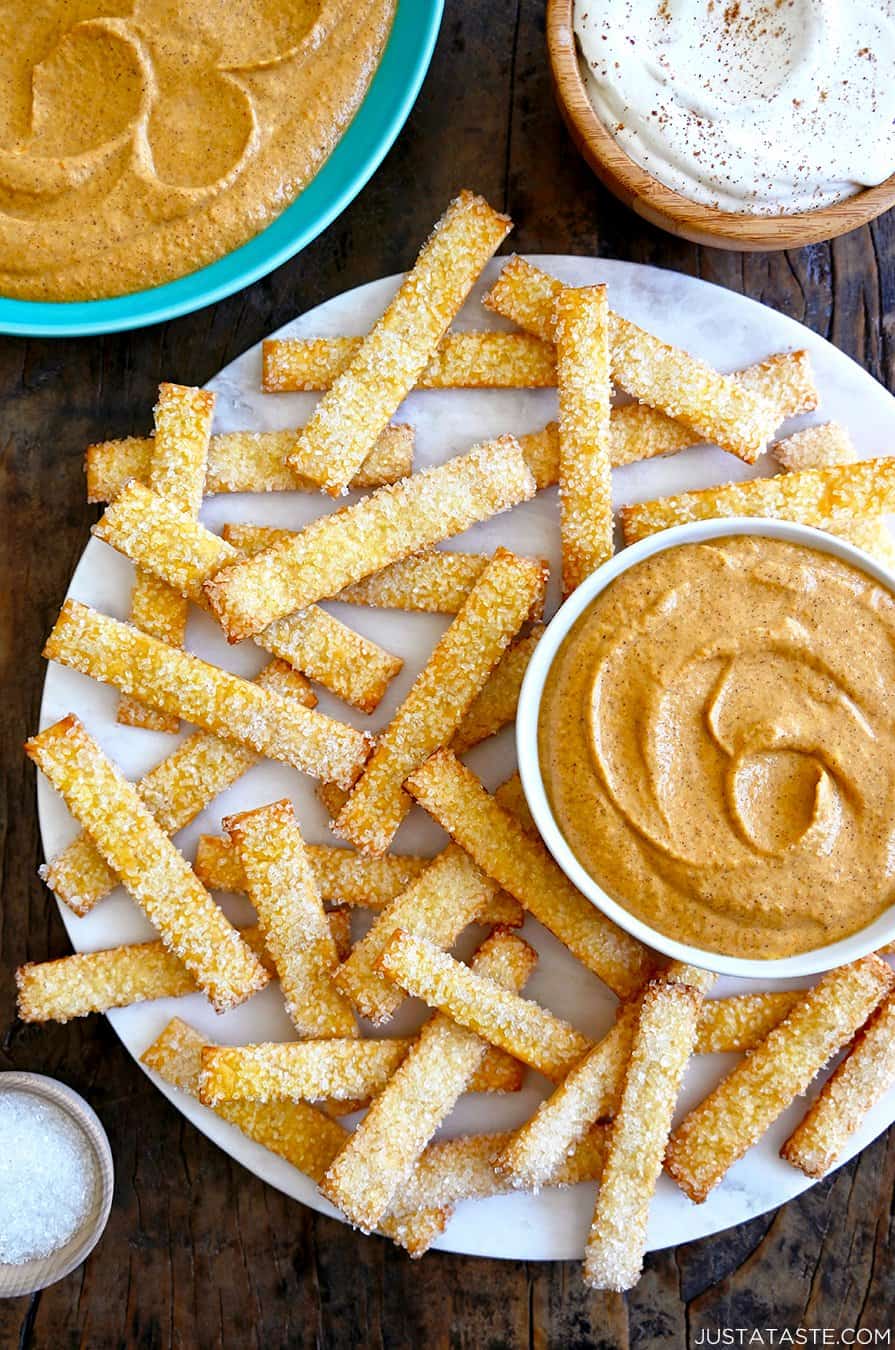 A top down view of pie crust fries on a white platter with bowls of pumpkin dip