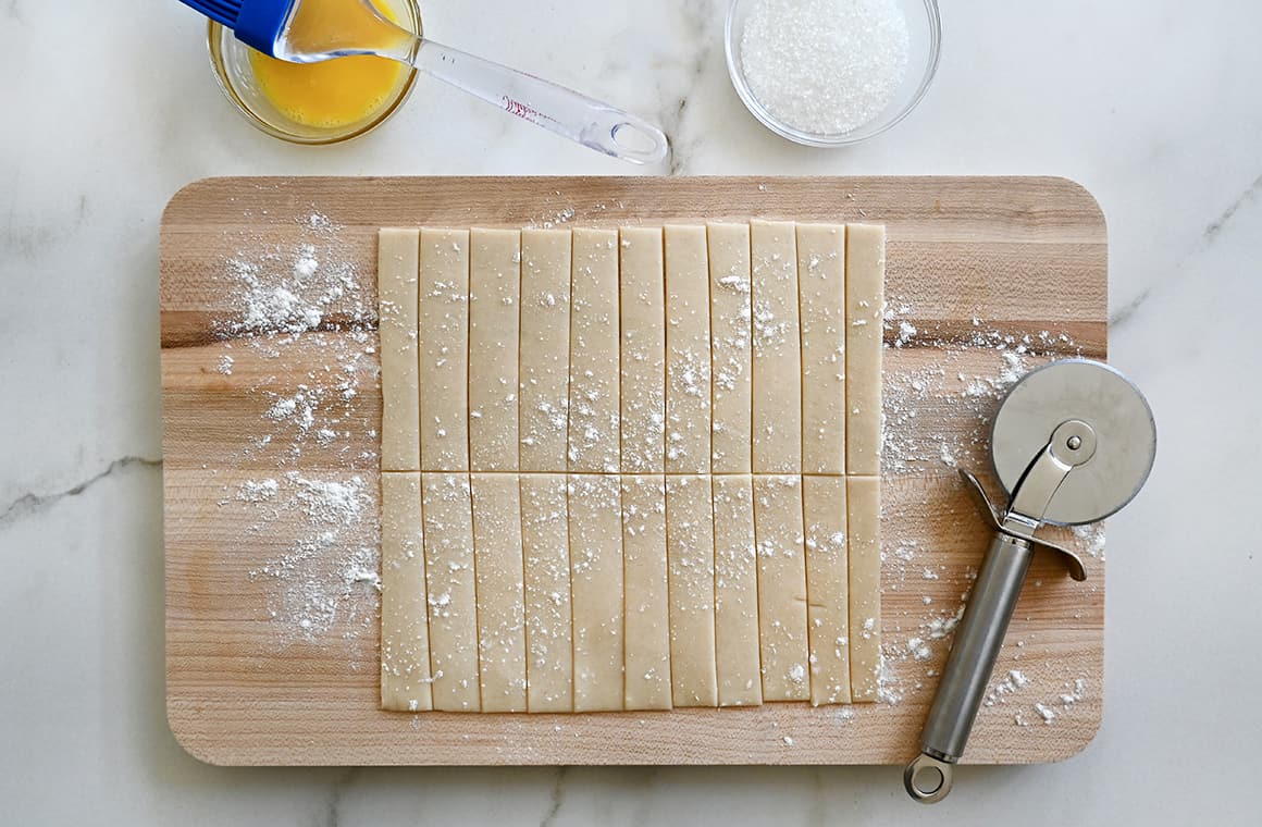 Unbaked pie dough cut into strips on a cutting board next to a pizza cutter