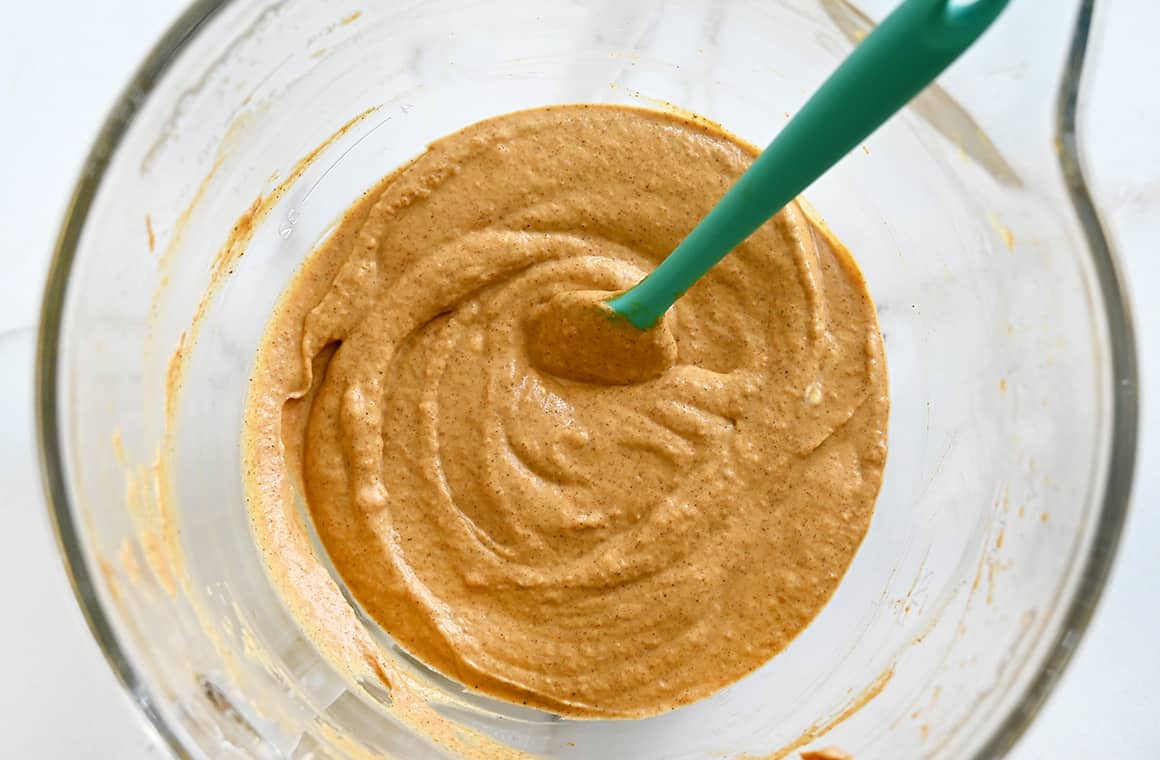 A top-down view of a clear bowl containing no-bake pumpkin dip and a teal spatula