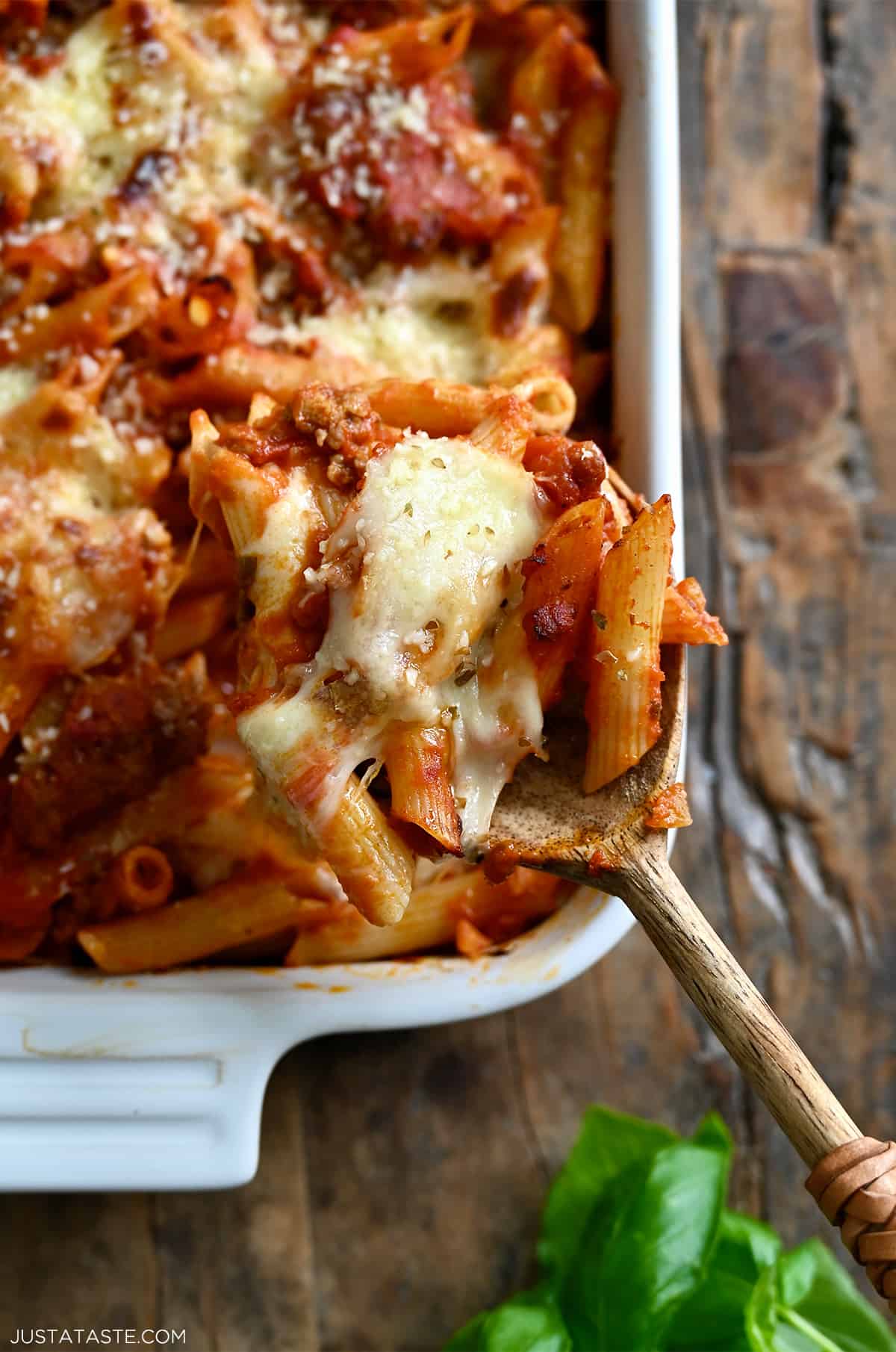 A spoon with baked penne pasta and gooey mozzarella cheese.