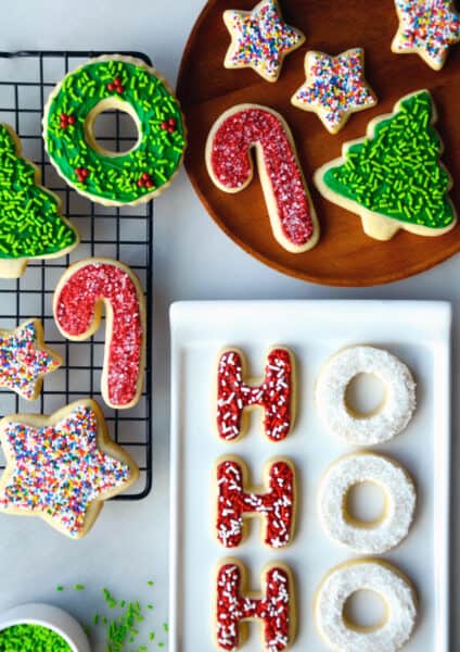Sugar cookies with frosting and sprinkles on a wire cooling rack, on a plate and on a white serving platter.