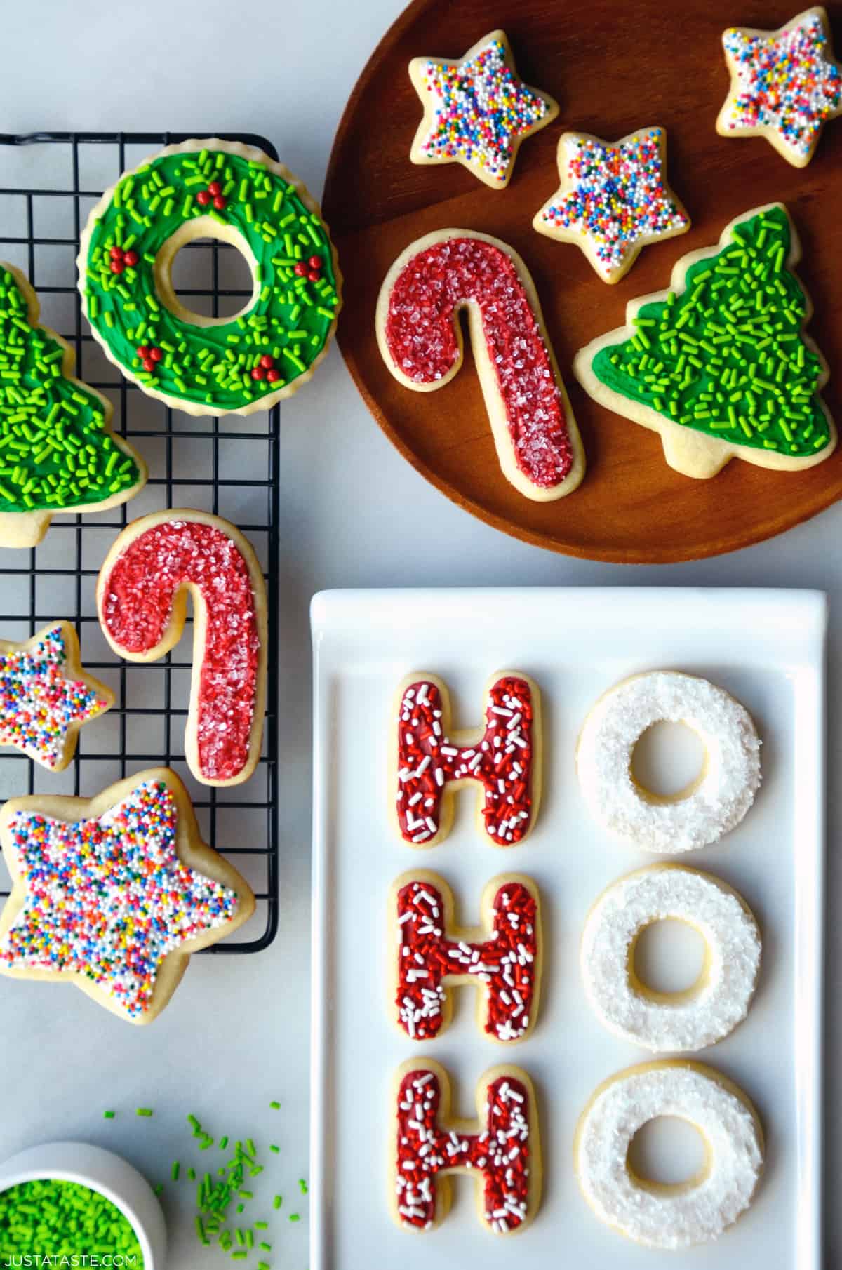 Sugar cookies with frosting and sprinkles on a wire cooling rack, on a plate and on a white serving platter.