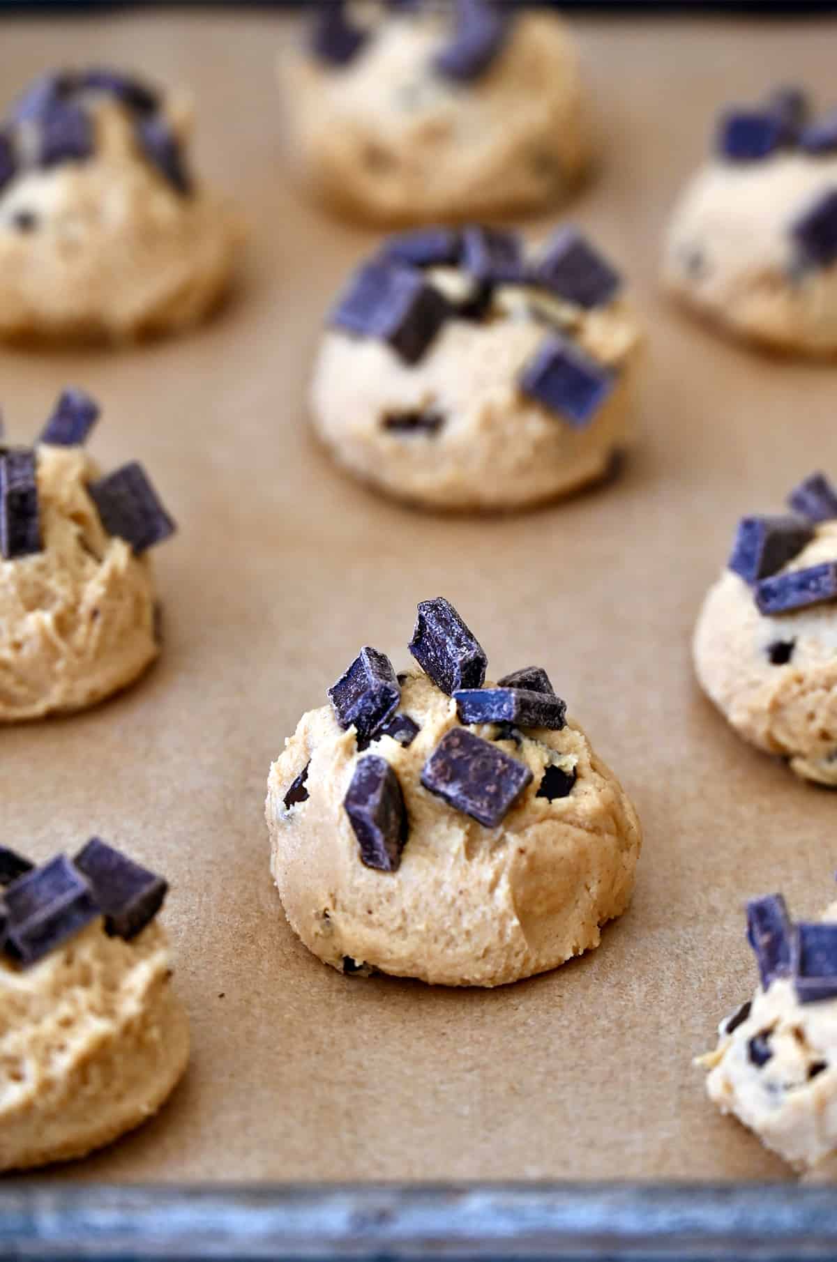 Balls of peanut butter cookie dough topped with chocolate chunks on a baking sheet lined with parchment paper.