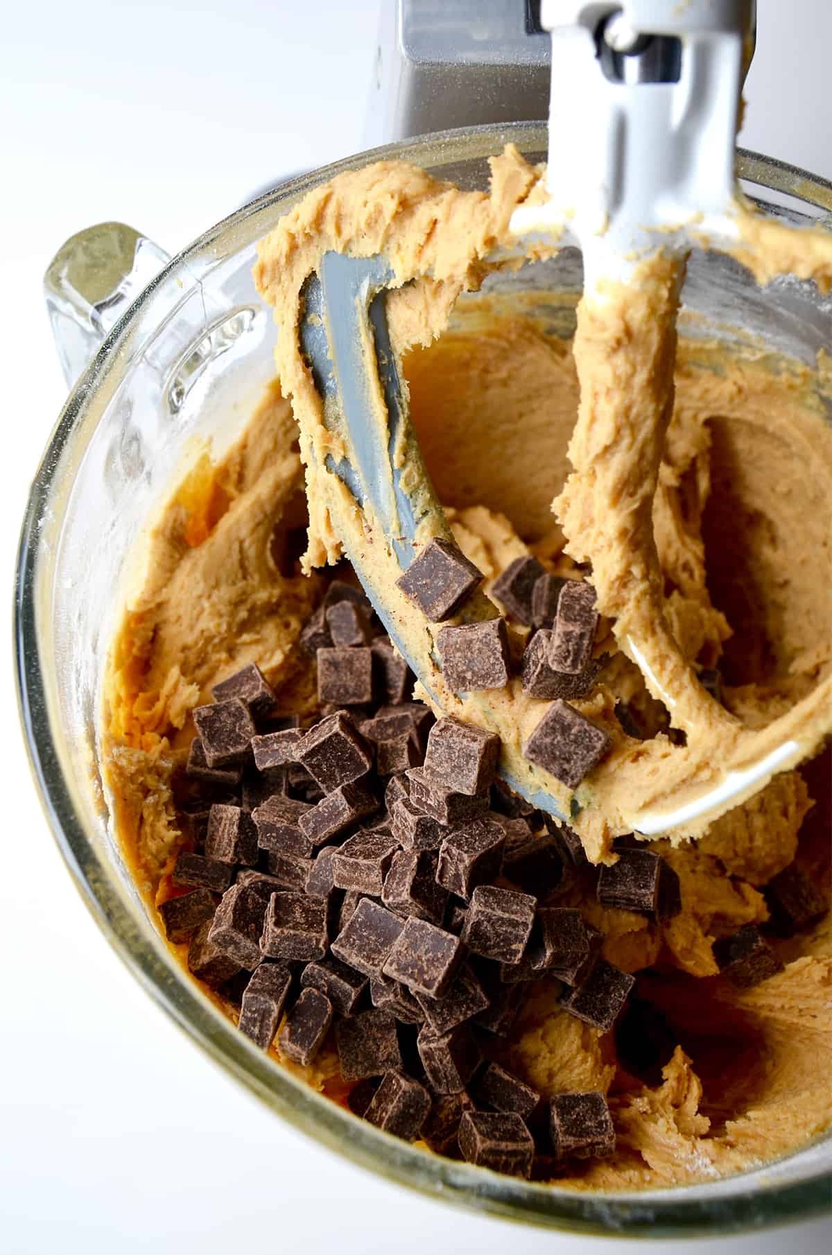 Peanut butter cookie dough topped with chocolate chunks in a stand mixer bowl with the paddle attachment.