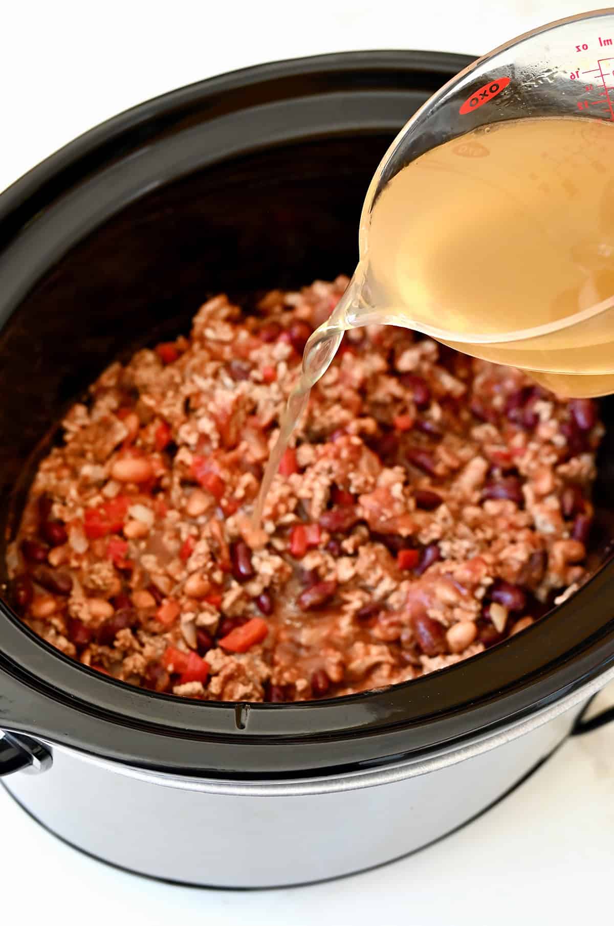 Adding chicken broth to a slow cooker with a ground chicken and bean mixture.