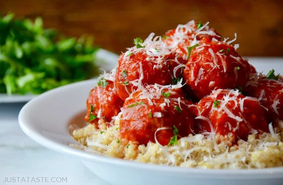 A white bowl containing quinoa and turkey meatballs with marinara sauce