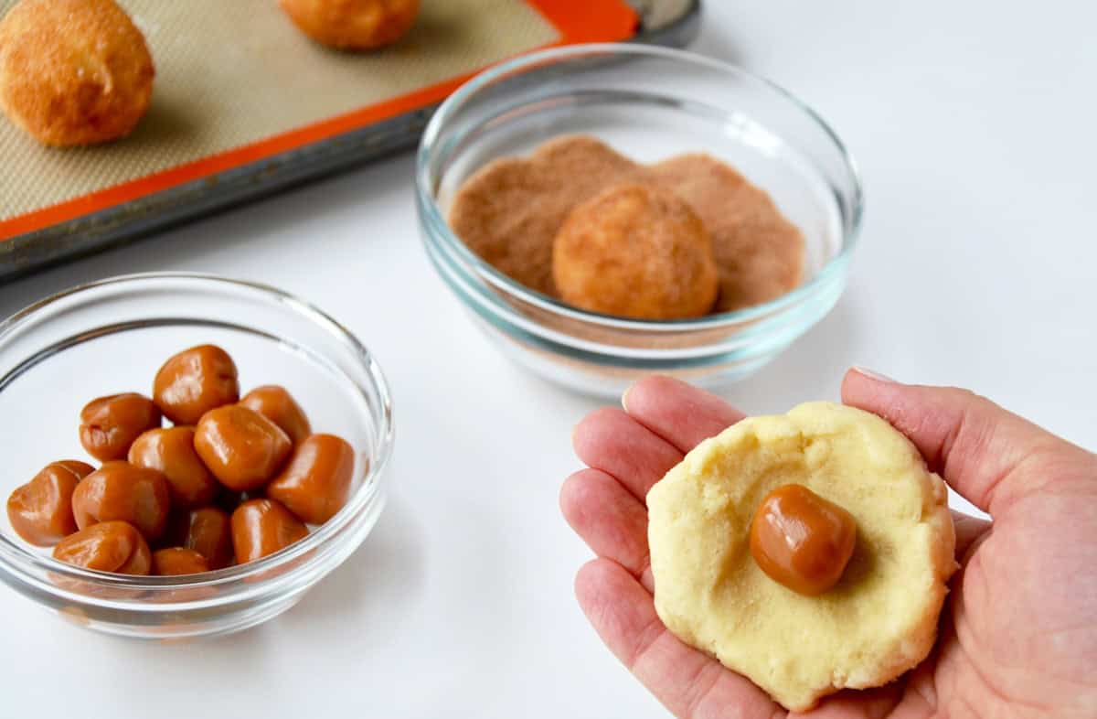 A soft caramel in the center of a snickerdoodle cookie dough ball before being sealed and rolled in cinnamon sugar.
