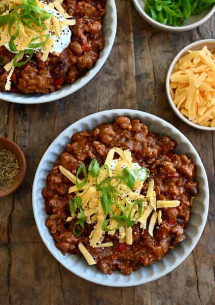 Two bowls containing slow cooker ground chicken chili topped with sour cream, shredded cheddar cheese and sliced scallions.
