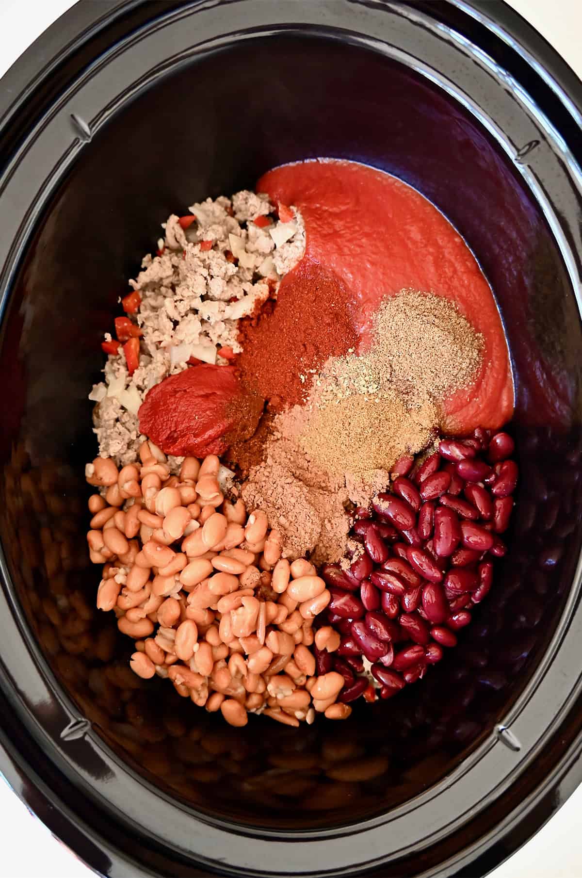 Browned ground chicken, kidney beans, pinto beans, tomato sauce, tomato paste and spices in a slow cooker.