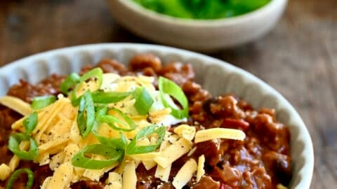 Healthy ground chicken chili topped with a dollop of sour cream, shredded cheddar cheese and sliced scallions in a bowl.