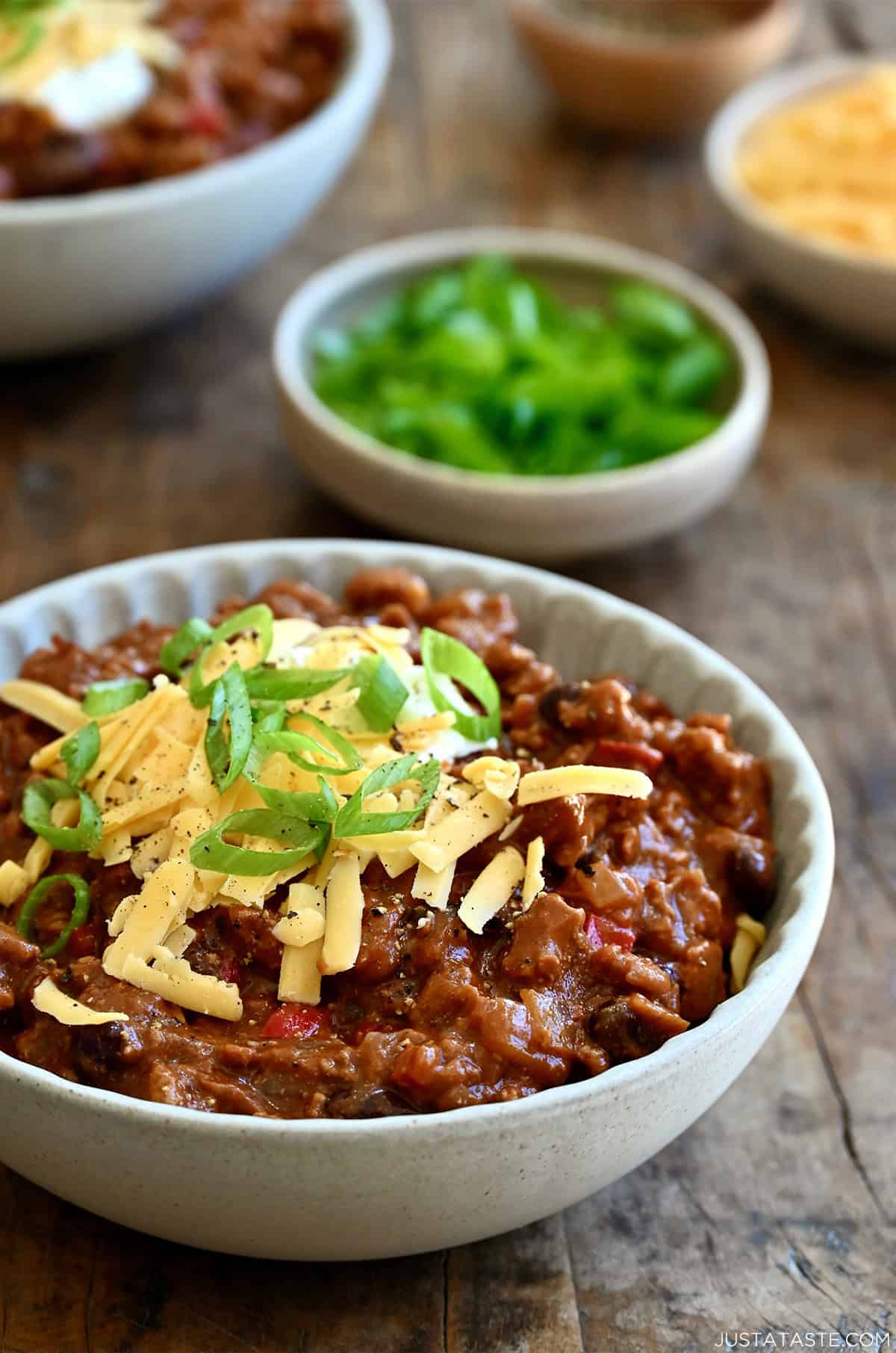 Healthy ground chicken chili topped with a dollop of sour cream, shredded cheddar cheese and sliced scallions in a bowl.