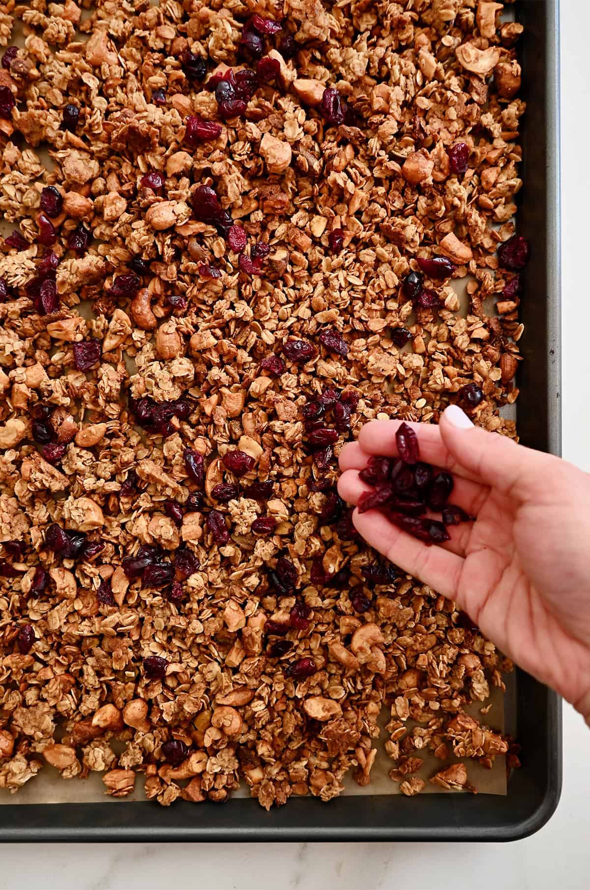 Adding dried fruit to baked granola on a sheet tray.