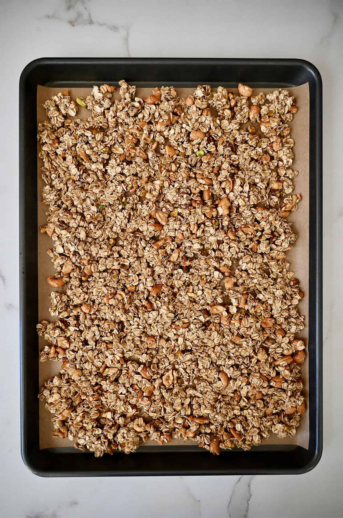 Deeply golden brown baked granola on a parchment paper-lined baking sheet.