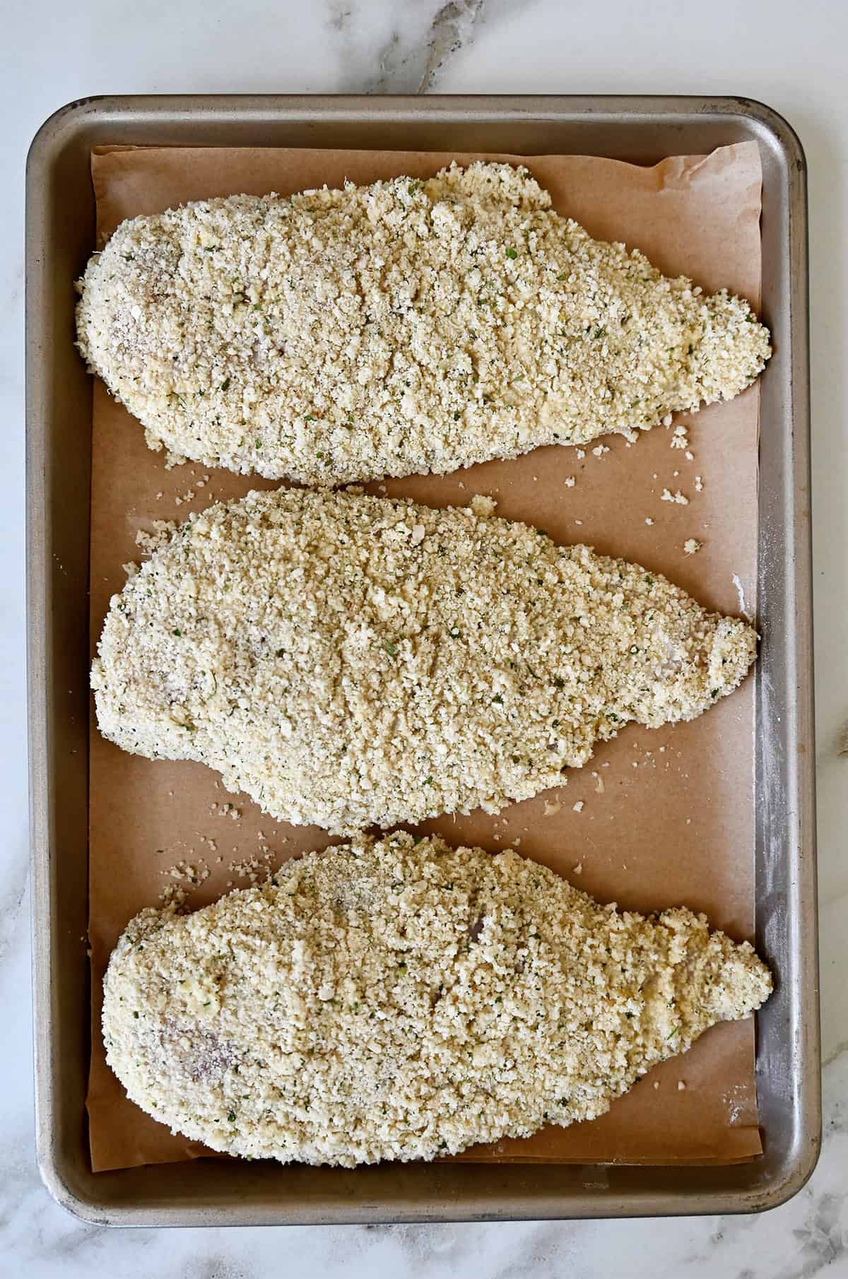 Panko breadcrumbs and Parmesan crusted chicken on a parchment paper-lined baking sheet.