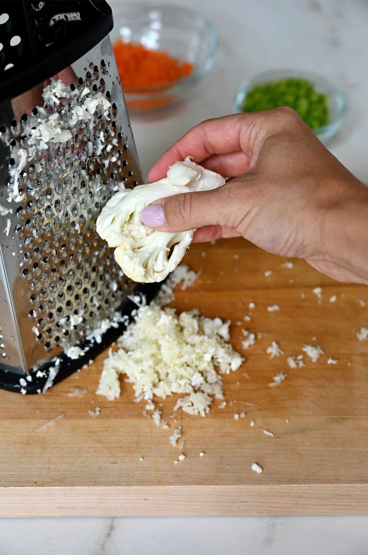 Grating a piece of cauliflower on a box grater.