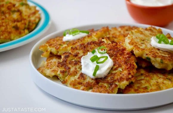 A white plate containing cauliflower fritters topped with sour cream and scallions