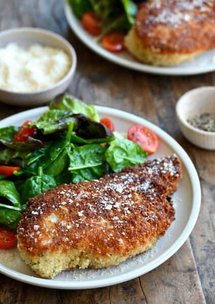 Parmesan herb crusted chicken breast on a plate with a simple Romaine and cherry tomato salad.