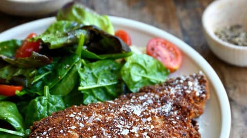 Parmesan herb crusted chicken breast on a plate with a simple Romaine and cherry tomato salad.