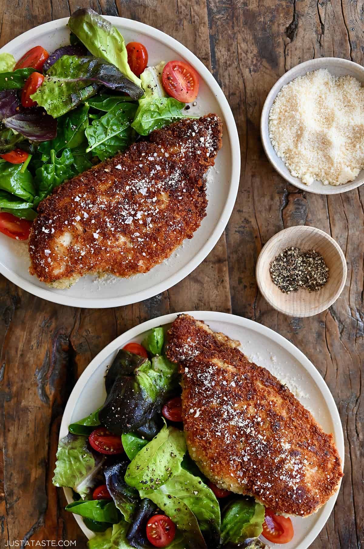 Two dinner plates with Parmesan Herb Crusted Chicken and a simple Romaine salad with halved cherry tomatoes.