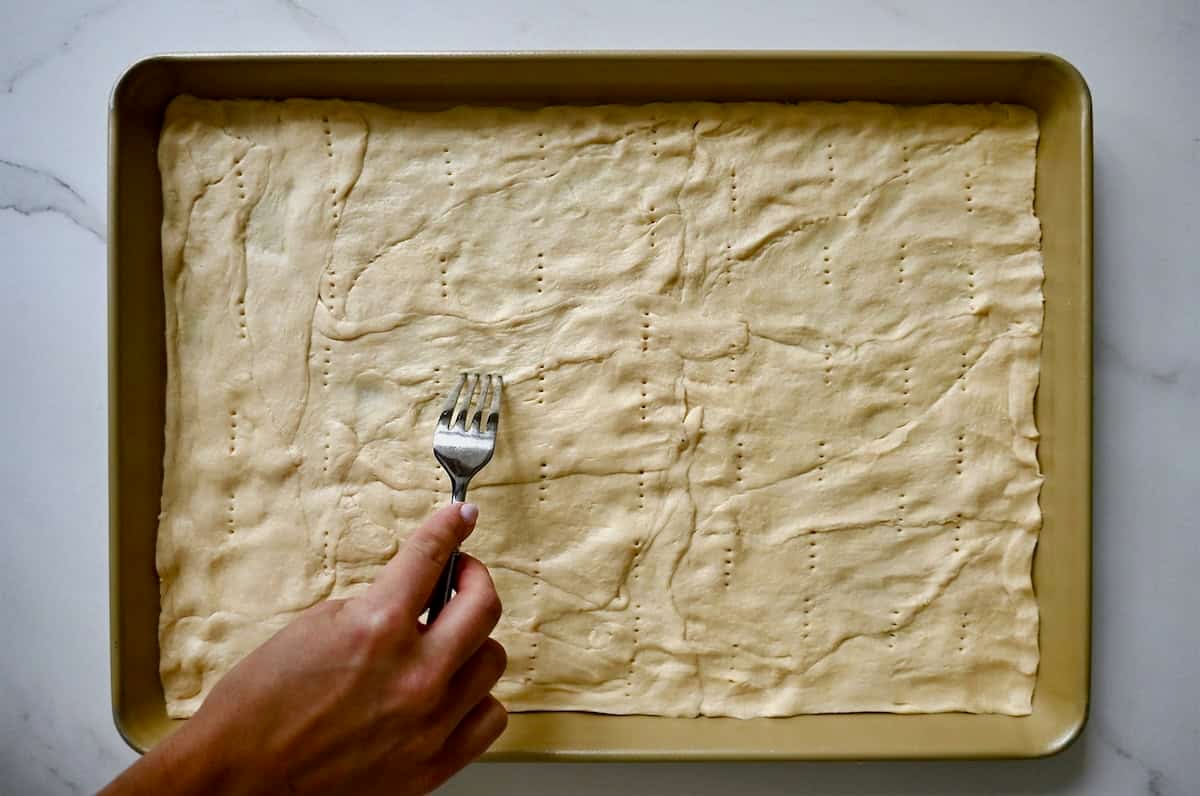 Pricking crescent roll dough with a fork.