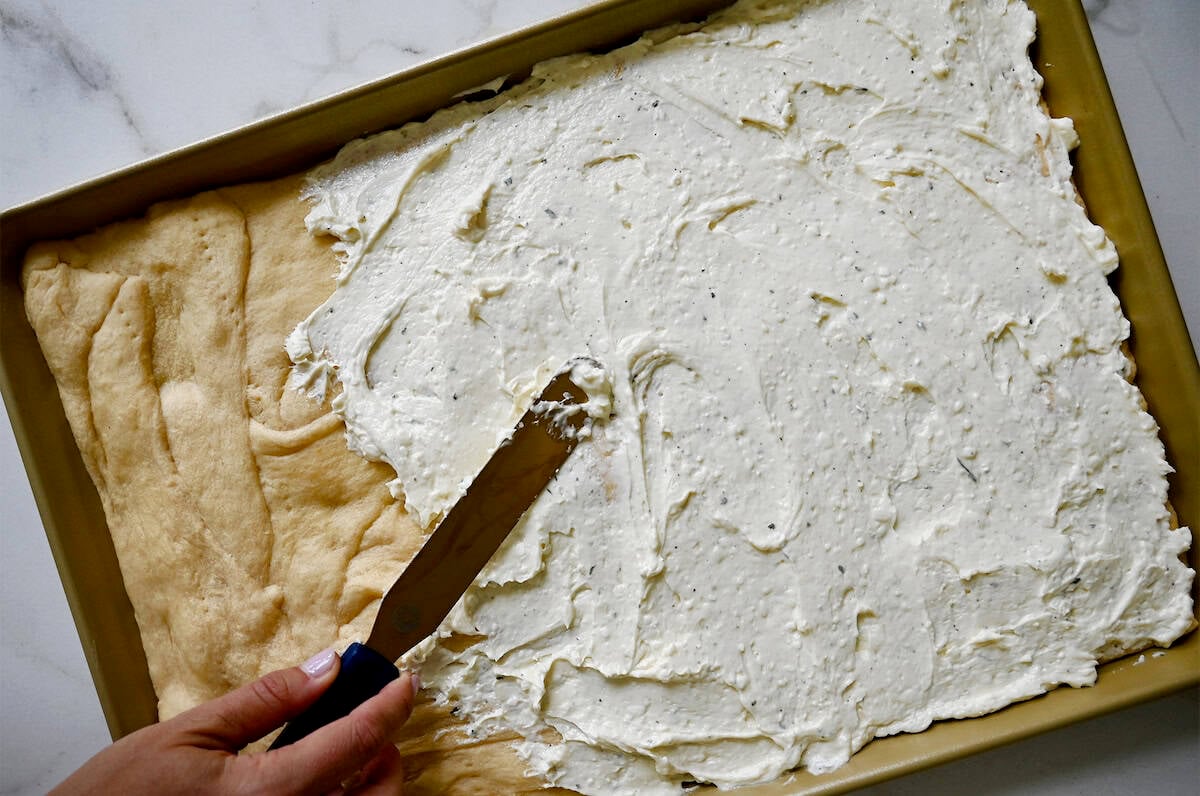 Spreading creamy Ranch and cream cheese spread atop baked crescent rolls on a baking sheet.
