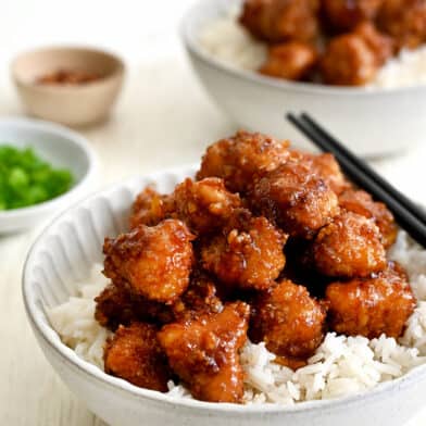 Baked Orange Chicken atop white rice in a bowl with chopsticks