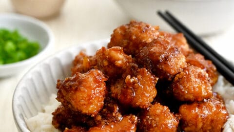 Baked Orange Chicken atop white rice in a bowl with chopsticks