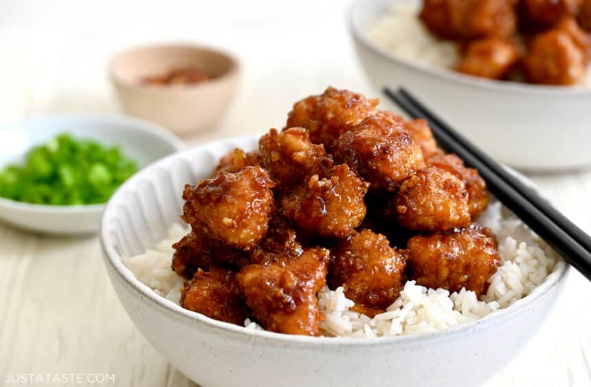 Chopsticks resting on the edge of a bowl that contains Air Fryer Orange Chicken and atop white rice