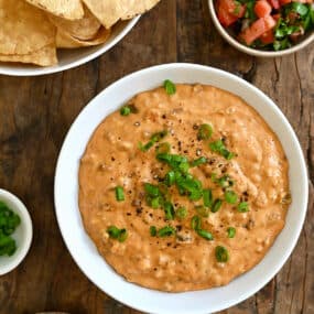 Chorizo queso dip in a white bowl next to a bowl filled with tortilla chips and a small bowl containing pico de gallo.