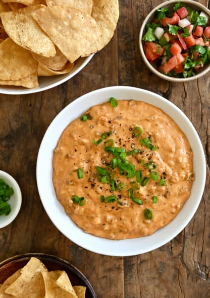 Chorizo queso dip in a white bowl next to a bowl filled with tortilla chips and a small bowl containing pico de gallo.