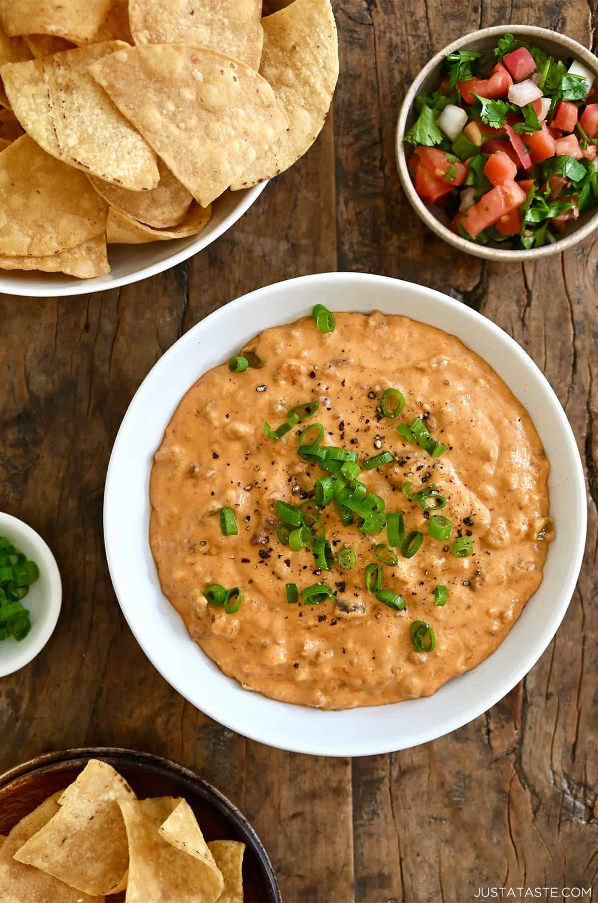 Chorizo queso dip in a white bowl next to a bowl filled with tortilla chips and a small bowl containing pico de gallo.