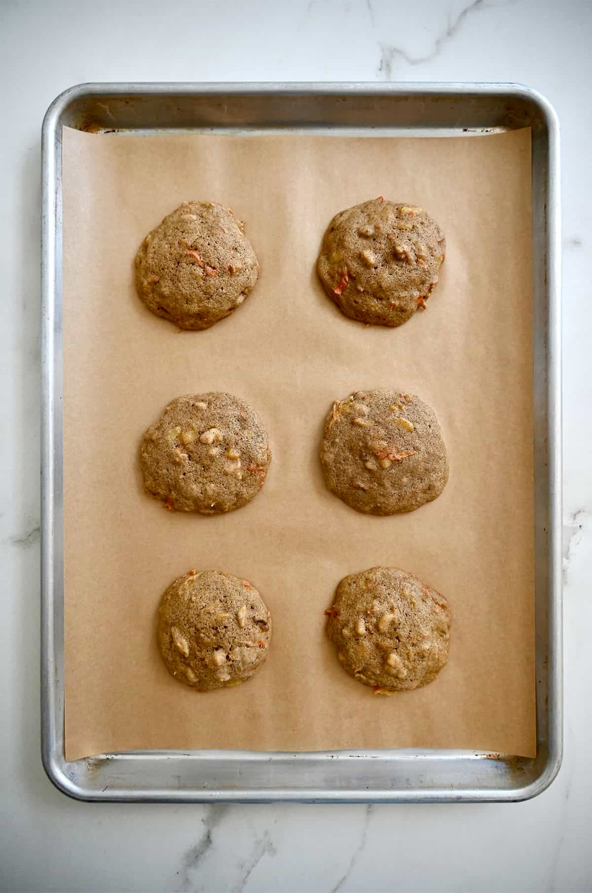 Freshly baked carrot cookies on a cookie sheet lined with brown parchment paper.