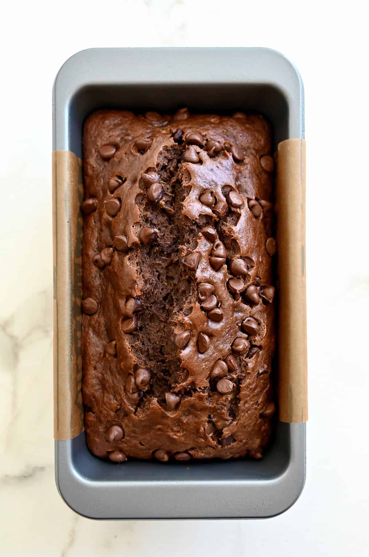 Baked chocolate banana bread loaded with chocolate chips in a bread pan lined with parchment paper.
