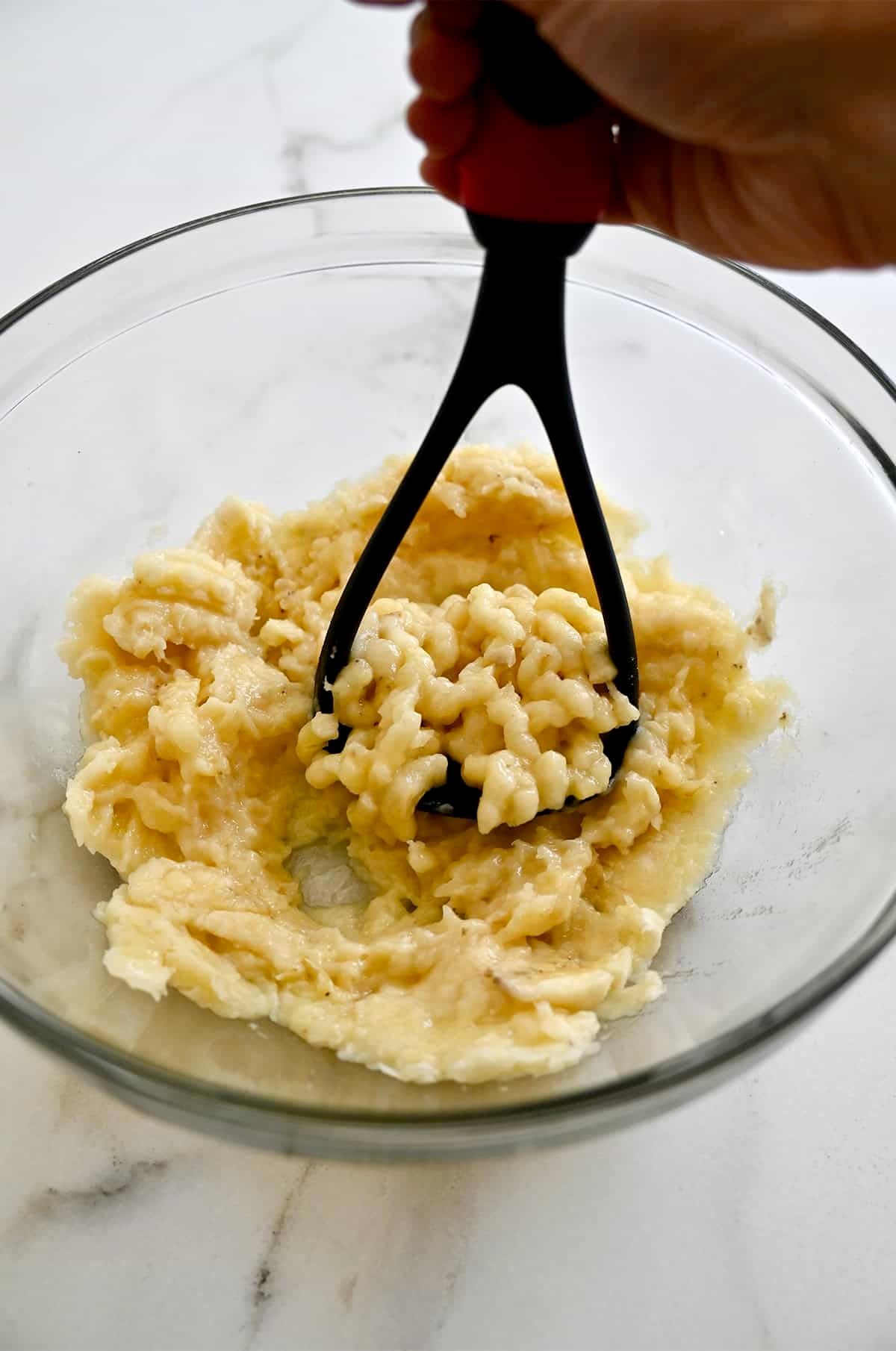 Mashing bananas with a potato masher in a large mixing bowl.