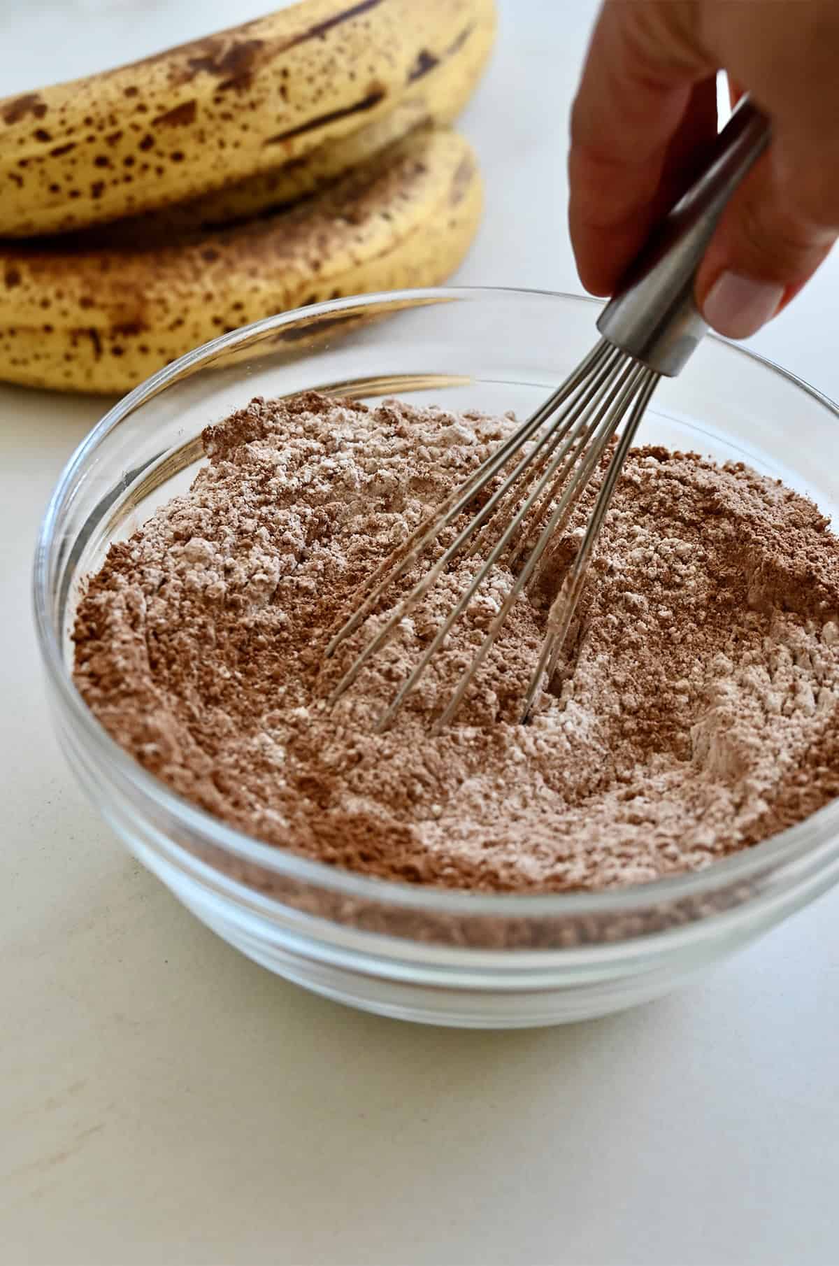 Flour, cocoa powder, sugar, baking powder, baking soda and kosher salt are being whisked together in a bowl.