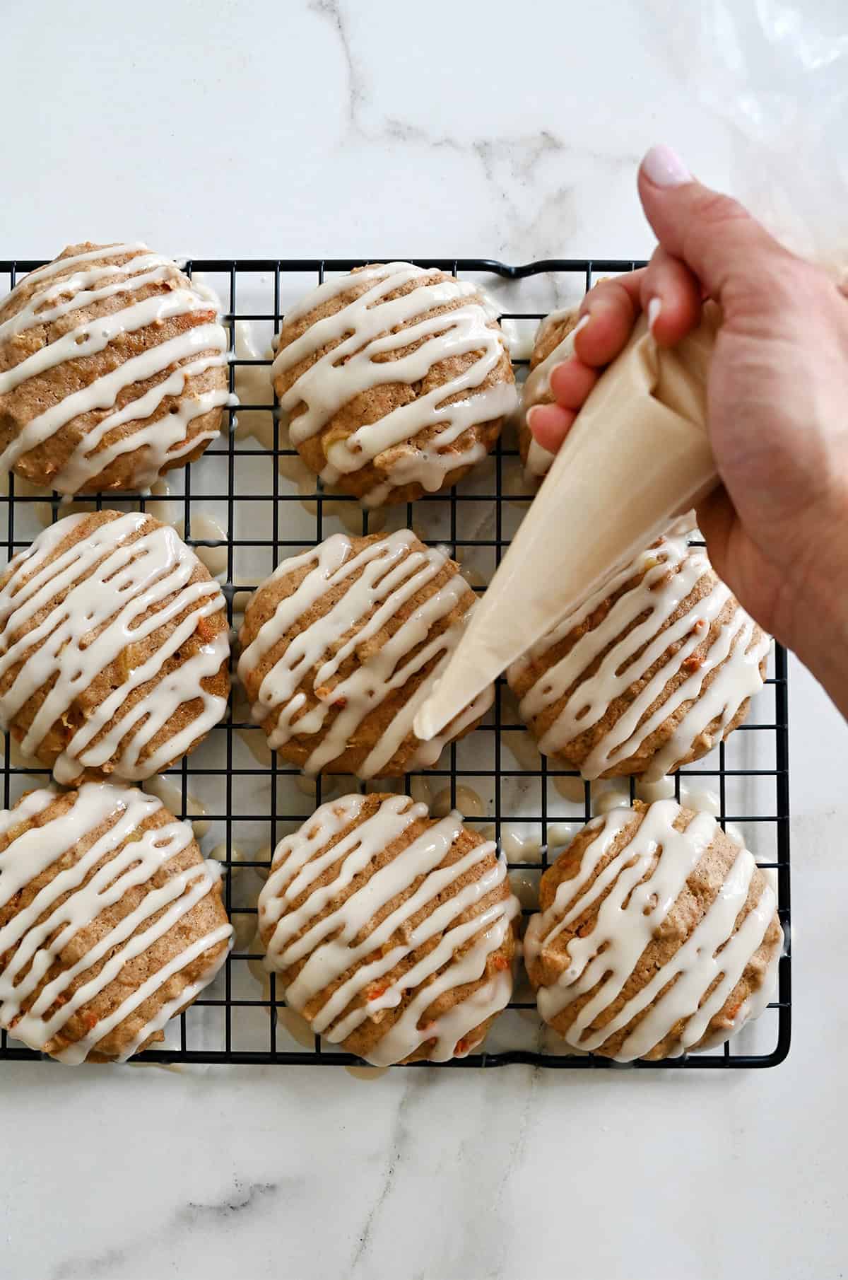 Piping cream cheese icing onto cooled carrot cake cookies on a wire rack.